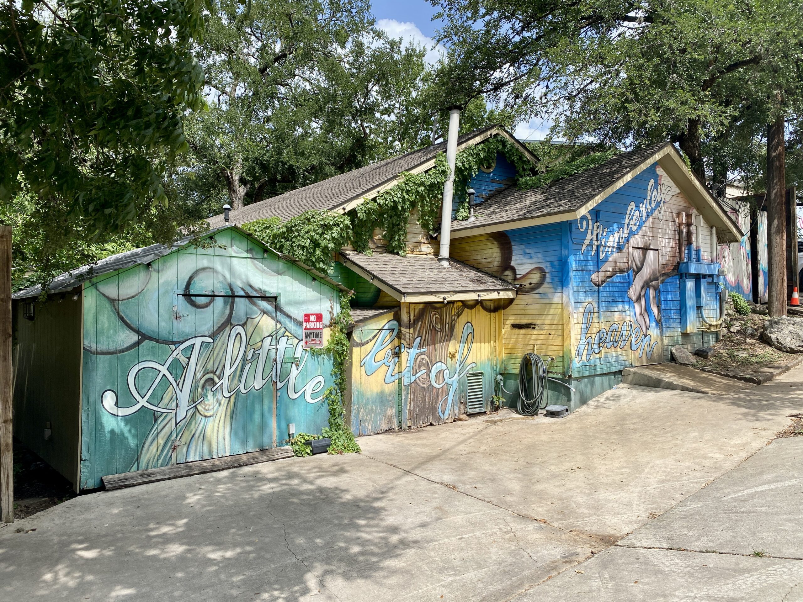 Colorful mural painted across wooden buildings reading "A little bit of Wimberley heaven" with a leaping deer illustration