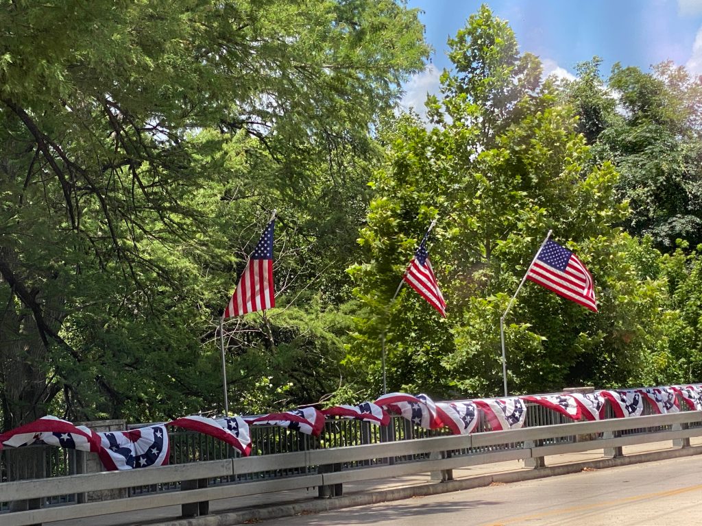 American flags and patriotic bunting decorating the bridge railing over Cypress Creek in Wimberley Texas