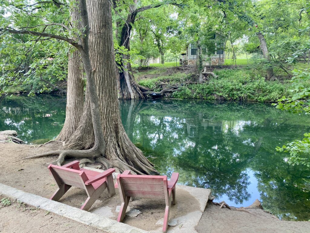 Two red chairs beside a large cypress tree at the edge of Cypress Creek in Wimberley Texas