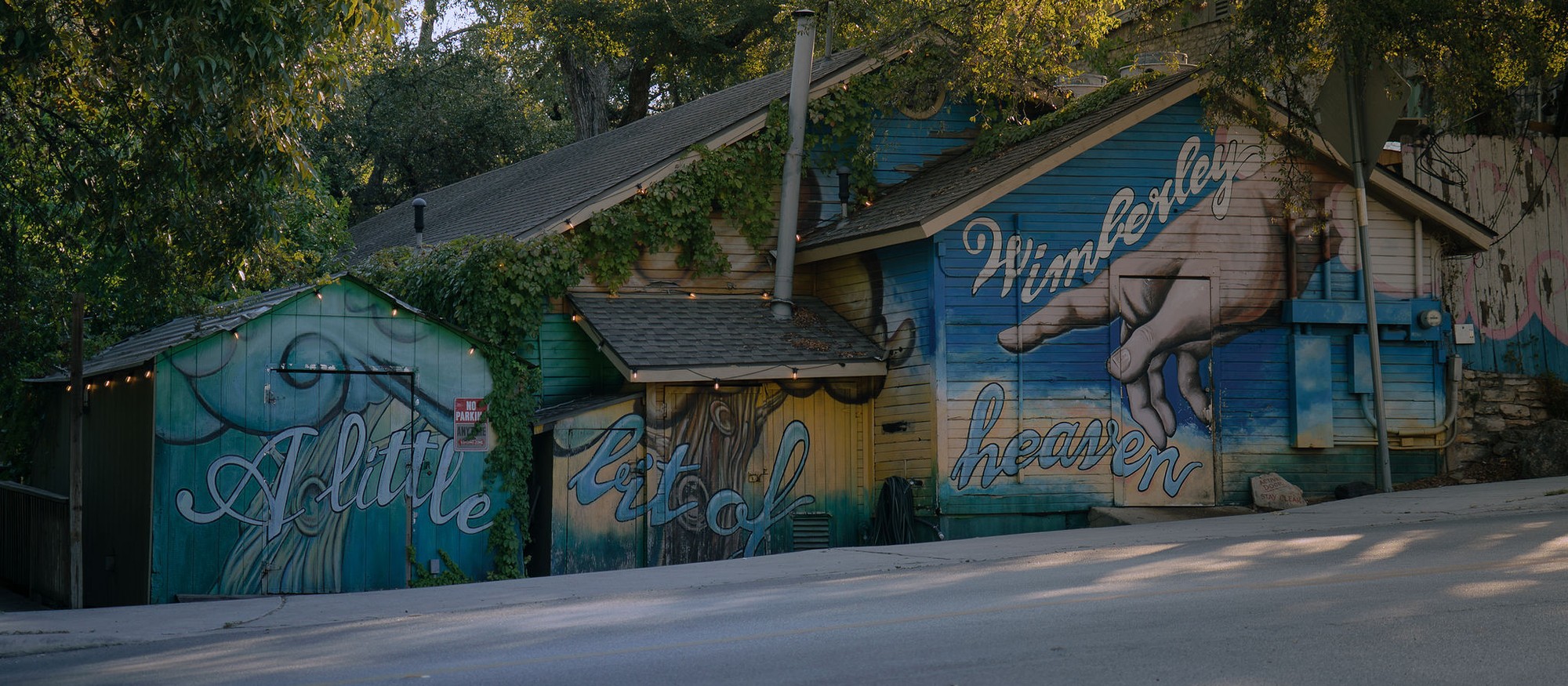 The colorful Wimberley mural beneath trees along a sunlit street.